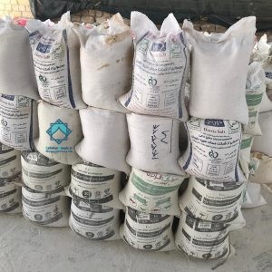 نمای نزدیک از چند کیسه 25 و 30 کیلویی پودر سفید قرار گرفته روی یکدیگر در فضای داخلی کارگاه